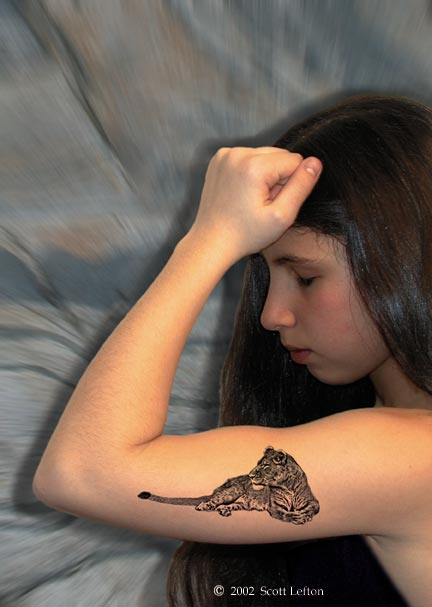 A young woman flexes her arm, with a tattoo of a lioness on her bicep.