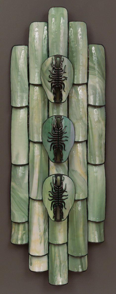 A sculpture made from rounded pieces of streaked green stained glass, including three cast bronze elements with an insectlike appearance.