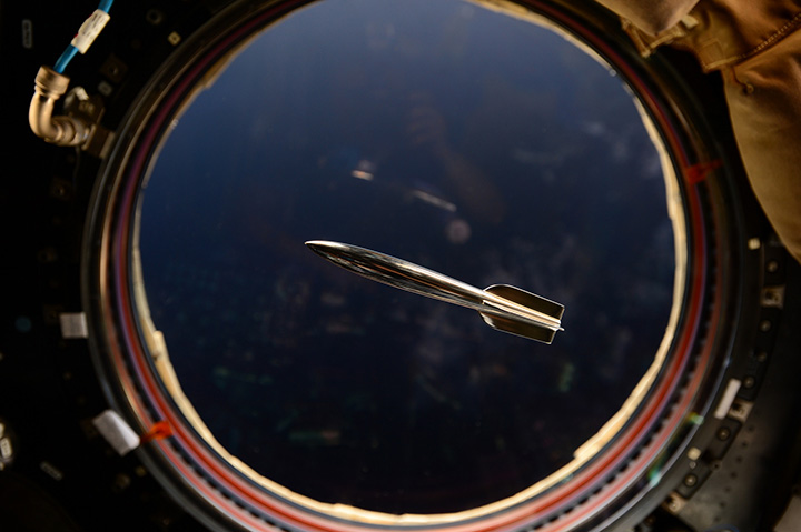 The Mini Hugo Rocket floats in the International Space Station in front of a window overlooking the Earth.