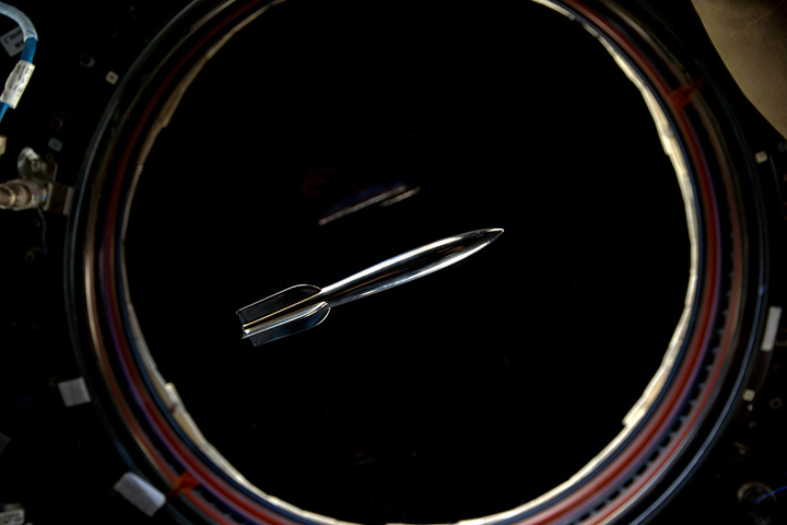 The Mini Hugo Rocket floats in the International Space Station in front of a window overlooking the Earth.